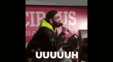 a man with a beard is singing into a microphone while sitting on a stage .