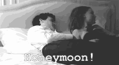 a black and white photo of a man and a woman laying in bed with the words `` honeymoon '' written above them .