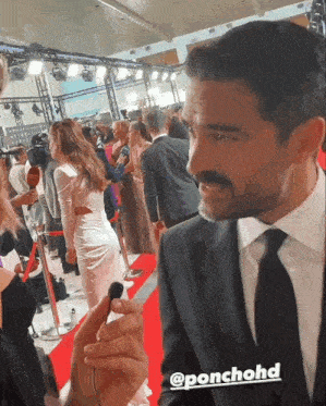 a man in a suit and tie is standing on a red carpet with the hashtag @ponchohd on the bottom