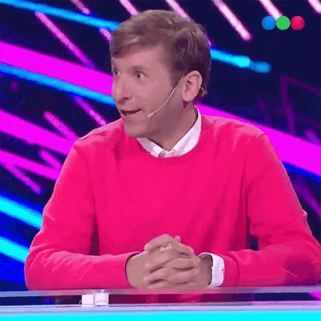 a man in a pink sweater is sitting at a table