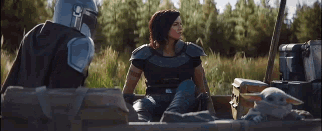 a woman in armor is sitting in a boat next to a child and a man in armor .