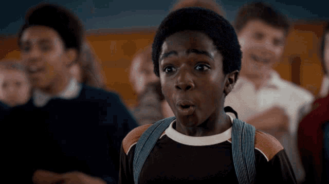 a boy with a backpack makes a surprised face in front of a group of children