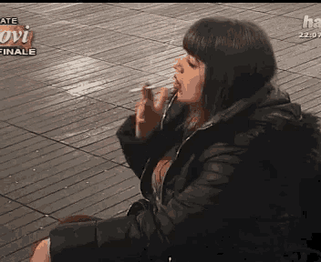 a woman is sitting on the ground smoking a cigarette in front of a sign that says " finale "