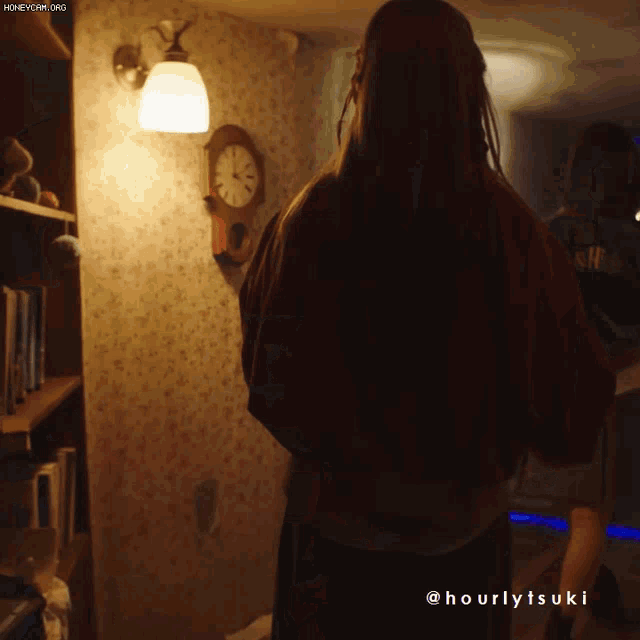 a woman is standing in a dark room with a clock on the wall and the words hourlytsuki on the bottom