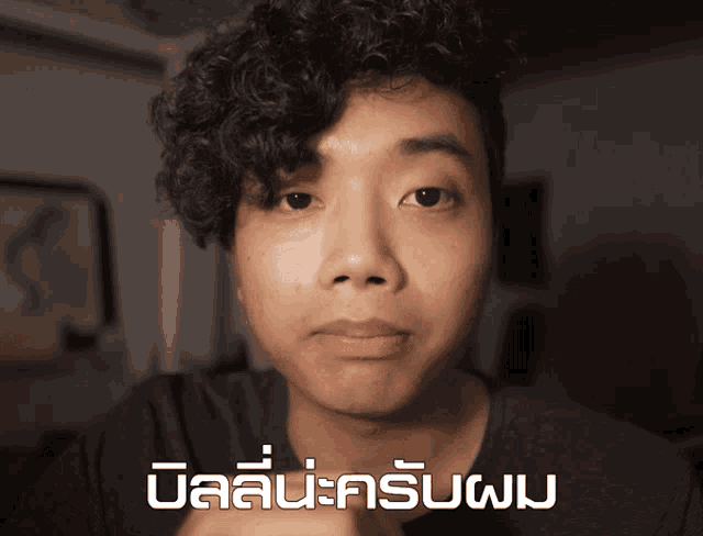 a man with curly hair looks at the camera with a foreign language written on the bottom right
