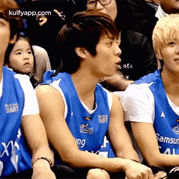 a group of young men are sitting in a stadium wearing blue basketball uniforms .