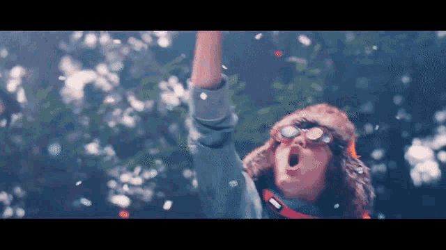 a man wearing a fur hat and goggles is standing in the snow with his arm in the air