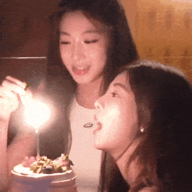 two young women are blowing out candles on a cake