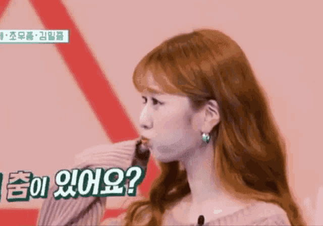 a woman with red hair is wearing a pink sweater and earrings and is looking at the camera .