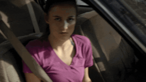 a woman in a purple shirt is sitting in the back of a car