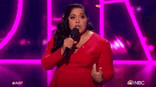 a woman in a red dress is standing in front of a microphone on a stage .