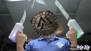 a man in a blue shirt is holding two swords in front of his face .