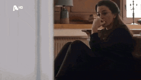 a woman is sitting on a couch with her hand on her chin and a hd logo in the corner .