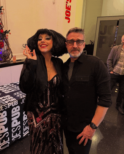a man and a woman are posing for a picture in front of a joe 's pub sign