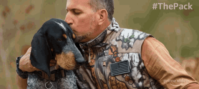 a man in a camo vest is kissing his dog