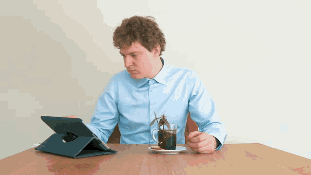 a man sits at a table with a tablet and a cup of green tea