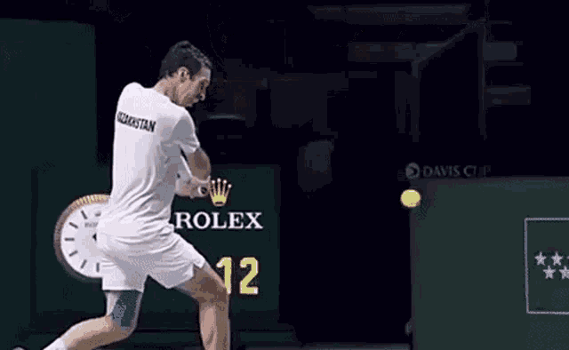 a man swinging a tennis racket in front of a rolex clock