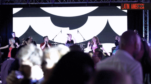 a group of people are dancing in front of a large screen that says latin american