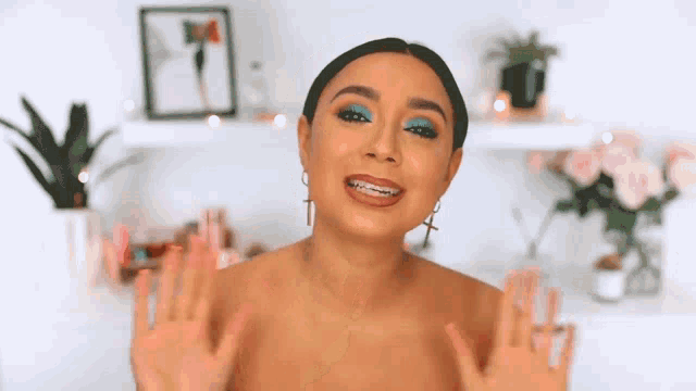 a woman with braces on her teeth is making a funny face while wearing blue eyeshadow and earrings .