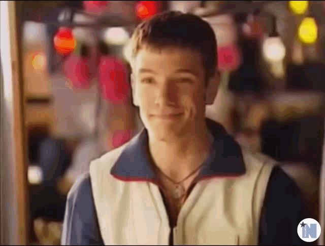 a man wearing a vest and a necklace is smiling in a blurry photo .