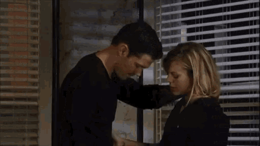 a man and a woman are kissing in front of a window in a room .