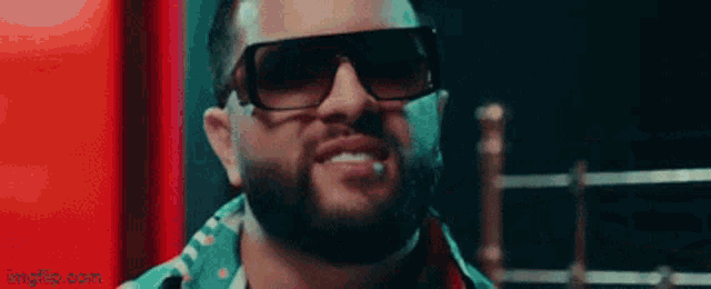 a man with a beard wearing sunglasses and a cigarette in his mouth is smiling .