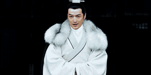 a man in a white robe with a fur collar smiles at the camera