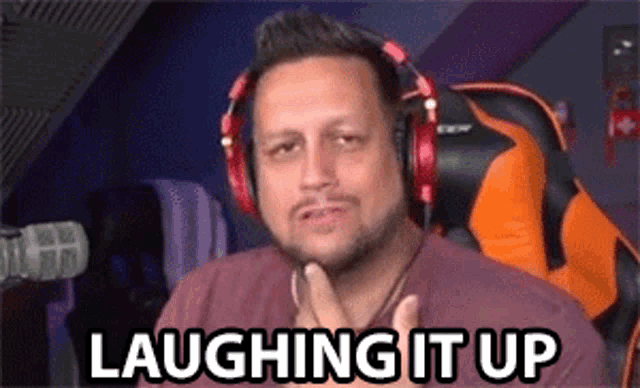 a man wearing headphones is laughing it up while sitting in a gaming chair .