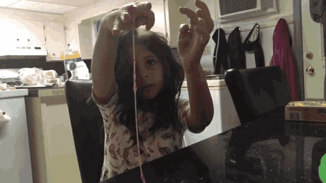 a little girl is sitting at a table playing with a pink string
