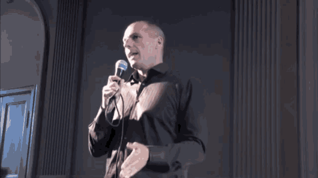 a bald man is holding a microphone and giving a middle finger