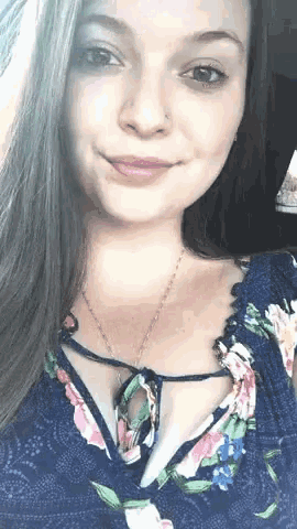 a woman wearing a floral top and a necklace smiles for the camera
