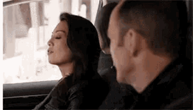 a man and a woman are sitting in the back seat of a car looking at each other .