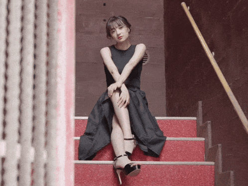a woman in a black dress sits on red stairs with her legs crossed