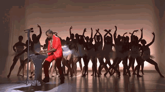 a man in a red suit stands in front of a podium surrounded by dancers