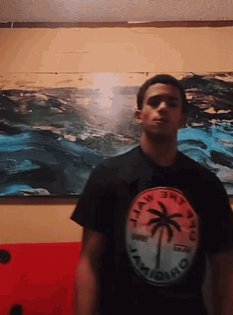 a man wearing a black shirt with a palm tree on it stands in front of a large painting