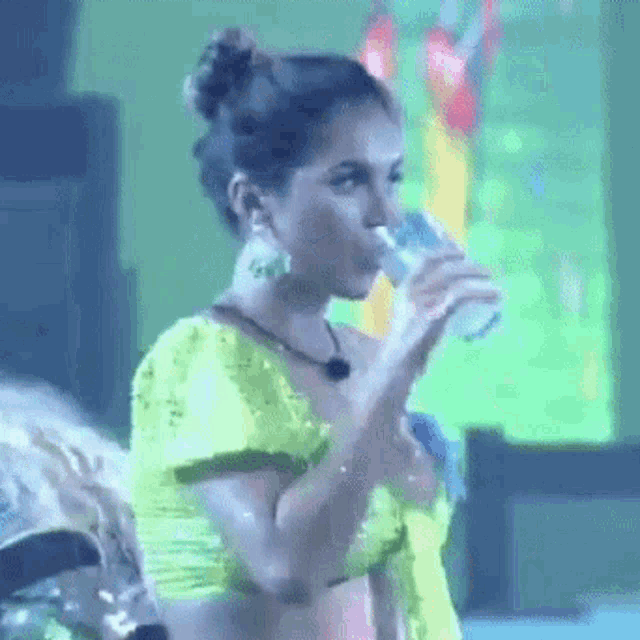a woman in a neon green top is drinking from a glass .