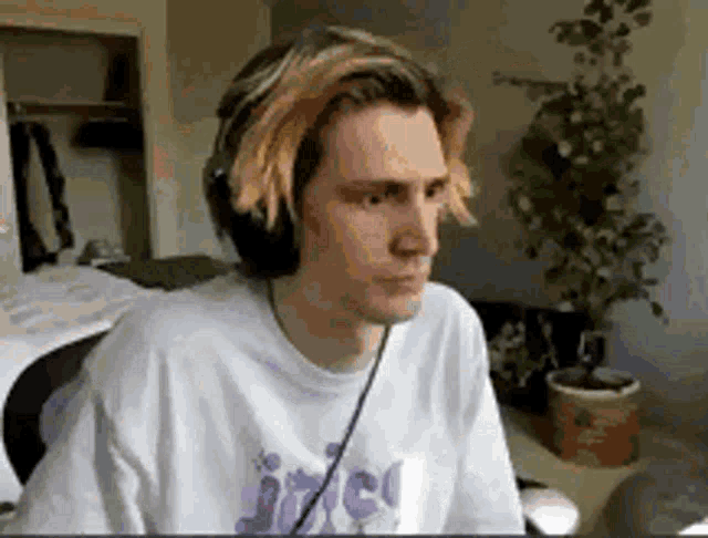 a young man wearing headphones and a white shirt is sitting in front of a computer screen .