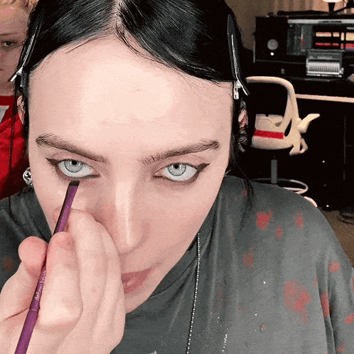 a woman applying eyeliner with a purple brush on her face