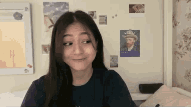 a woman is sitting in front of a wall with posters on it and a picture of vincent van gogh on it .