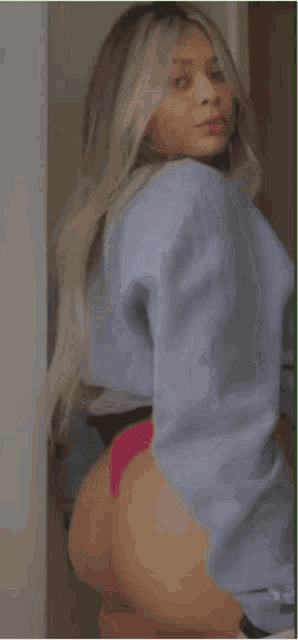 a woman wearing a blue sweater and pink underwear is standing in a doorway .