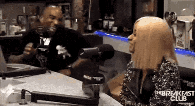 a woman is sitting at a table talking into a microphone while a man looks on .