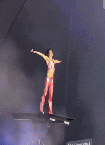 a woman in red pants is standing on a platform with her arms outstretched