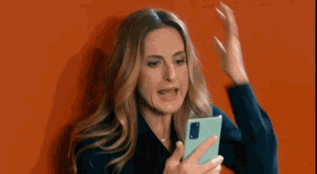 a woman is making a funny face while looking at her cell phone .