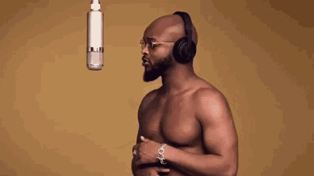 a shirtless man is singing into a microphone with headphones .