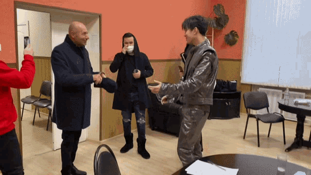 a man in a leather jacket shakes hands with another man in a black hoodie