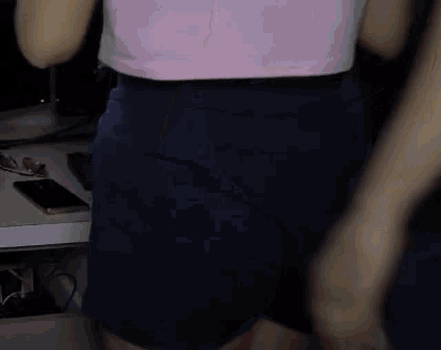 a woman in a pink shirt and blue shorts is standing in front of a computer desk .