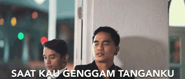 two men are standing in front of a door with the words saat kau genggam tanganku on the bottom