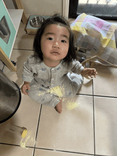 a baby is sitting on a tiled floor next to a trash can that has the word pasta on it