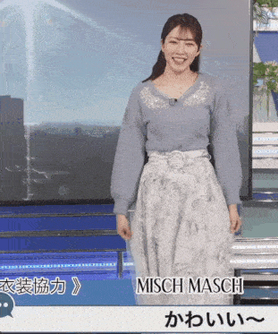 a woman wearing a blue sweater and a white skirt is standing in front of a screen that says misch maschi