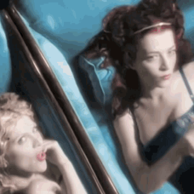 a woman with red hair is laying on a blue bed next to another woman